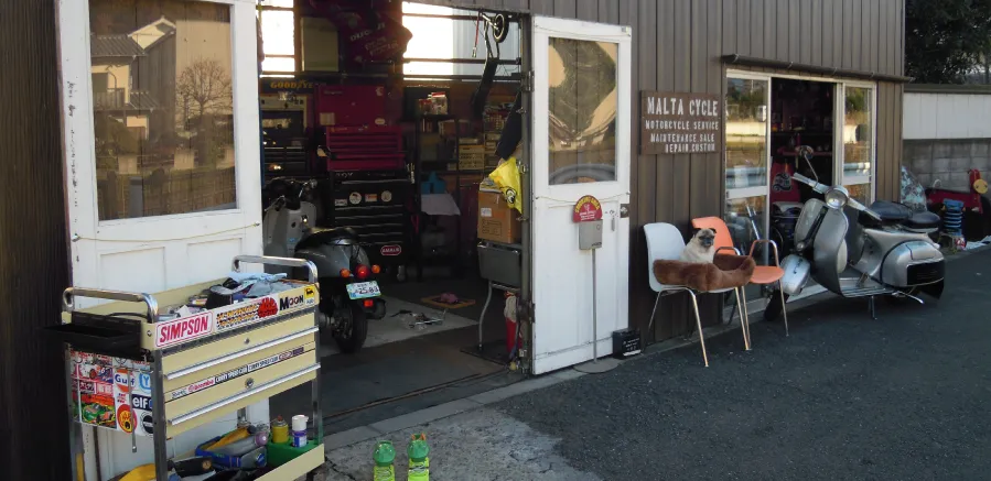 マルタサイクルの店舗外観。入口前にベンチとスクーターが並ぶ